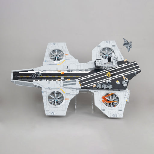 A toy model on a display stand of a LEGO Helicarrier, featuring a white and gray hull with black flight deck markings, orange accent details, and a small gray fighter jet attached to the rear